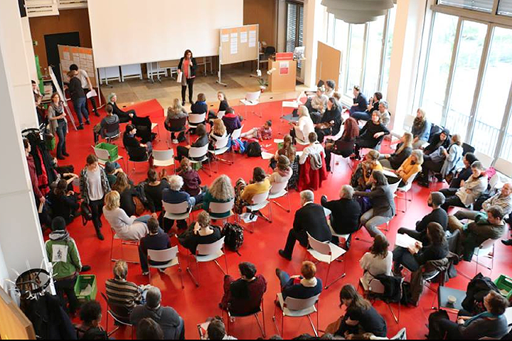Das Audimax der ASH Berlin von oben: etwa 30 Personen sitzen im Saal, eine Moderatorin auf der Bühne scheint eine Diskussion zu leiten.