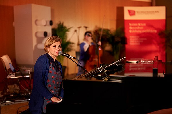 Bernadette La Hengst sitzt am Flügel und singt ins Mikrofon
