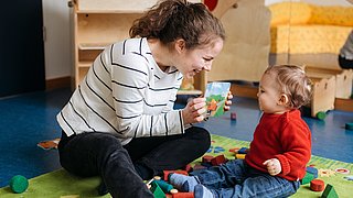 Eine Mutter zeigt ihrem Kind ein Bilderbuch , beide lächeln.