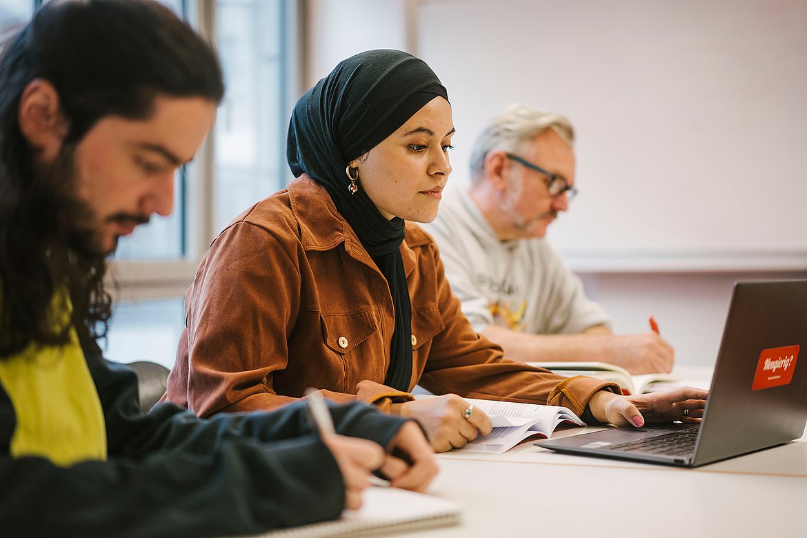 Drei Studierende sitzen in einem Seminar an einem Tisch.