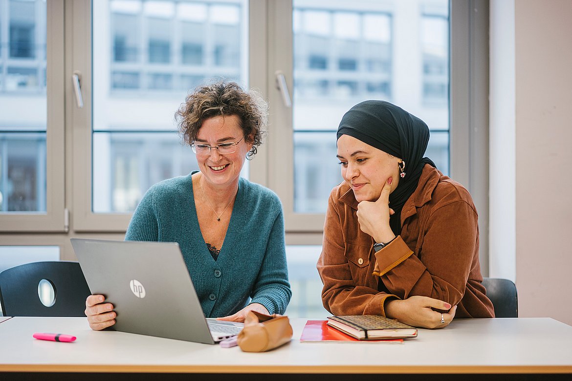 Zwei Frauen sitzen vor einem Laptop.