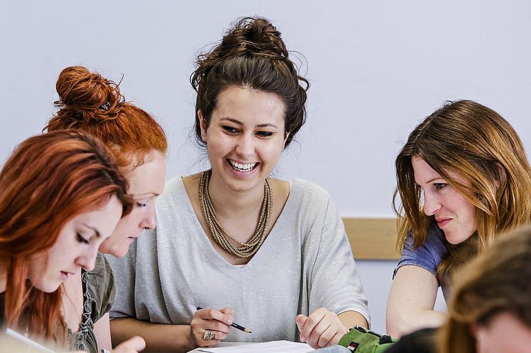 Drei Studentinnen des Master of Arts Studiengangs Biografisches und Kreatives Schreiben sitzen an einem Tisch und machen Notizen.
