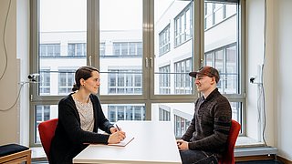 Eine Frau berät einen Mann. Sie sitzen sich gegenüber und wirken ausgelassen.
