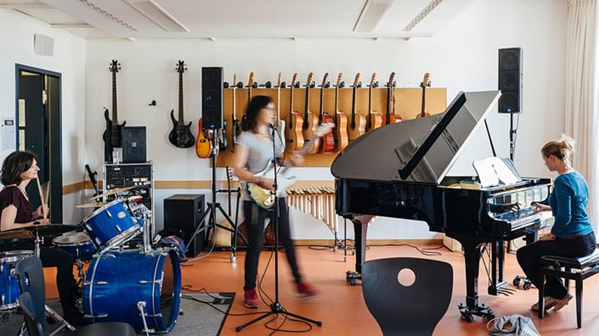 E-Gitarre, Schlagzeug und Flügel- eine Gruppe Studierender musiziert zusammen.